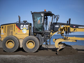 A road grader smooths the dirt road in Alaska.
