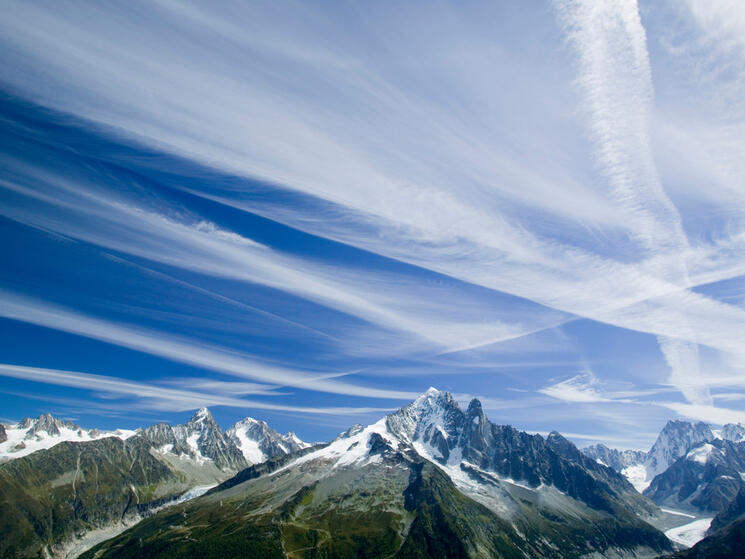 Tall mountains with blue sky above. White vapor trails streak across the blue sky.