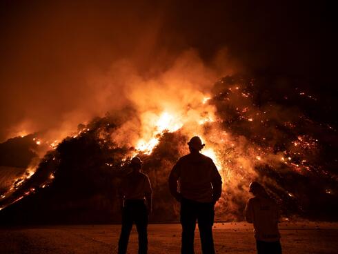 Firefighters fight a large fire burning in the hills.