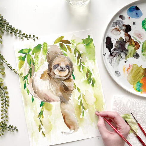 Photo of a painting of a sloth on a table with palette and artist's hand