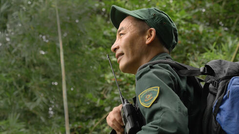 Profile portrait of a man in a green uniform with a hand radio looking off into a forest