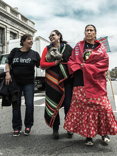 Three Indigenous women walk arm in arm down a main road in Washington, DC at the People's Climate March.