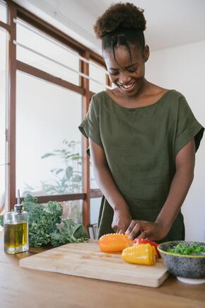 A woman stands in a kitchen chopping peppers